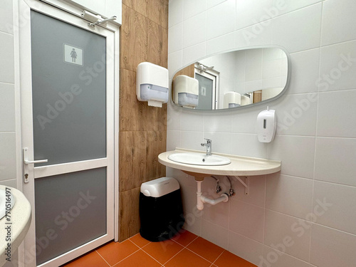 single sink in small public toilet with wall soap dispenser and paper towlels