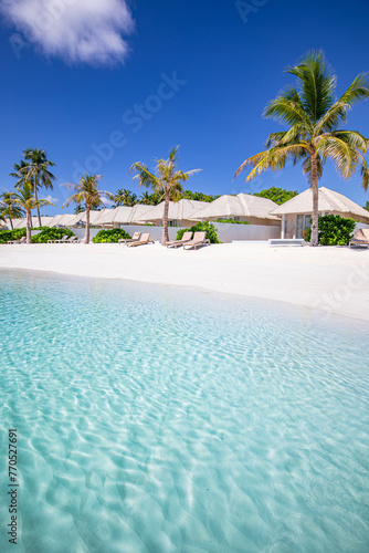 Beach villas in Maldives, luxury summer travel and vacation background. Amazing blue sea and palm trees under blue sky. Tropical landscape and exotic beach. Summer holiday or honeymoon destination