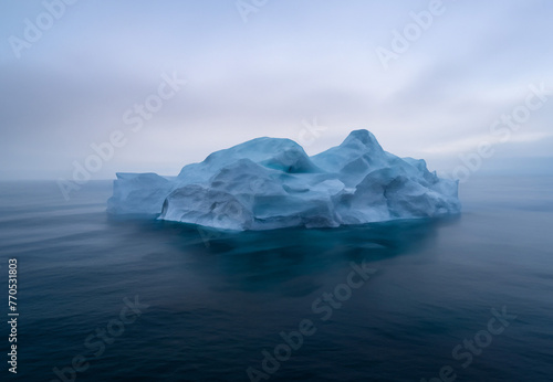 A massive iceberg, sculpted from a glacial landscape, floats in a cold, blue ocean under a clear Arctic sky, symbolizing the effects of climate change.