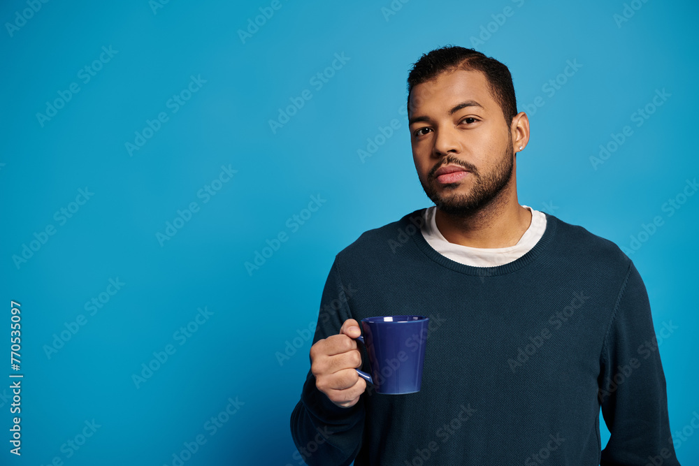portrait of attractive african american man in his 20s holding cup in hand against blue background portrait of attractive african american man in his 20s holding cup in hand against blue background