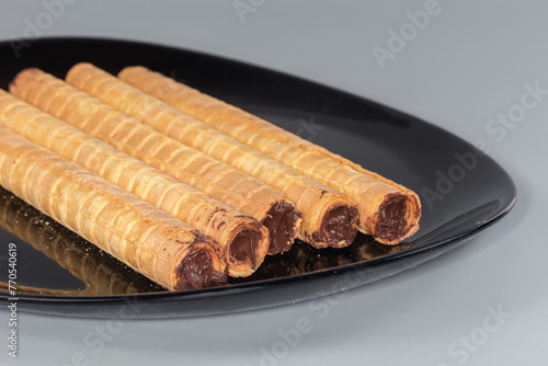 Wafer tubes with chocolate cream on black dish close-up photo