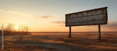 A tranquil natural landscape with a billboard standing tall in a field as the sun sets behind the horizon, casting a golden glow on the clouds and sky