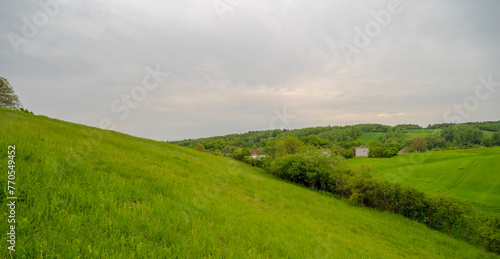 Mała wioska w dolinie wśród trawiastych wzgórz w Górach Świętokrzyskich. Pochmurne niebo nad piękną okolicą (koło Ostrowca) w wiosenne popołudnie.