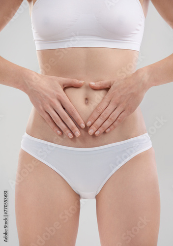 Woman, hands and stomach for wellness in studio, heart and body for diet and holistic gut health. Digestion, weight loss and abdomen detox for female person, self care for balance on background © peopleimages.com