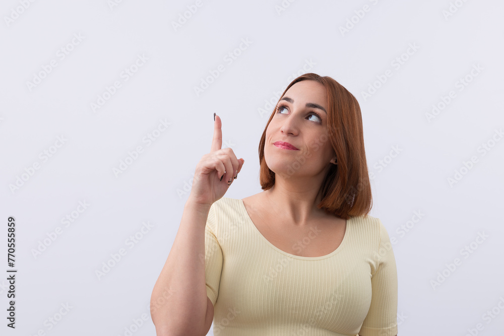 Studio portrait of pretty woman looking and pointing her finger up isolated on white background. Copy space. Promotion and marketing concept Studio portrait of pretty woman looking and pointing her finger up isolated on white background. Copy space. Promotion and marketing concept