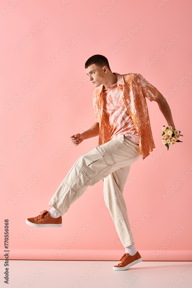 Full length image of fashionable man in layered outfit holding flowers on pink backdrop Full length image of fashionable man in layered outfit holding flowers on pink backdrop