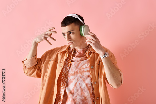 Portrait of man in layered outfit with wireless headphones dancing to music on pink backdrop