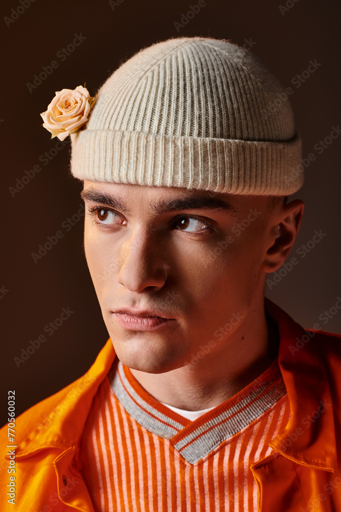 Portrait of handsome man in orange outfit wearing beige beanie with flower on brown background Portrait of handsome man in orange outfit wearing beige beanie with flower on brown background