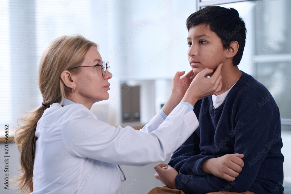 Side view portrait of female pediatrician examining young boy during health check up in clinic Side view portrait of female pediatrician examining young boy during health check up in clinic