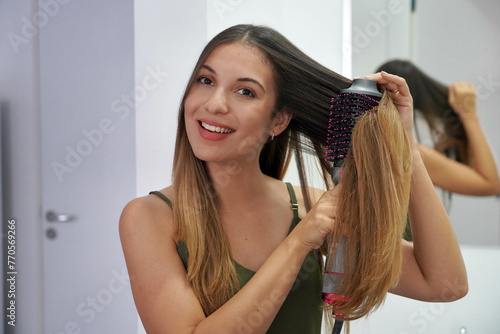 Portrait of young woman using round brush hair dryer to style hair in an easy way at home. Girl with electric blowout brush hair dryer. Hot air hair brush concept.