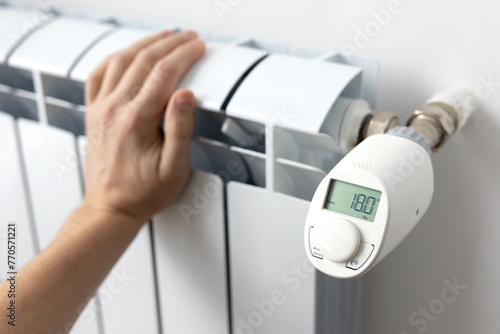 Hand touches the white heating battery in the apartment, I feel the temperature of the water in the heating system and the air in the room. Electronic thermostat. Preparation for spring and winter.