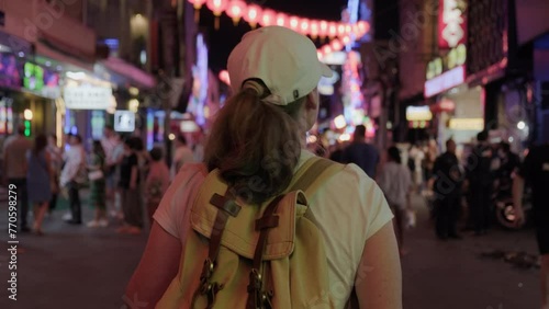Woman tourist walking along night street among crowd of people.