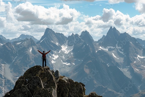 A lone hiker stands with arms raised in victory on the summit of a rugged mountain