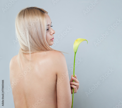 Female back with necklace and flower. Young woman with make-up and long blonde hair against white studio wall background