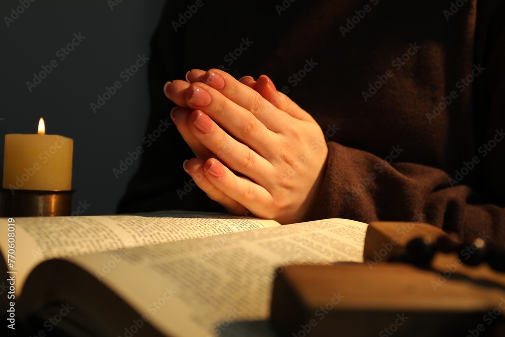 Obraz premium Woman praying at table with burning candle and Bible, closeup