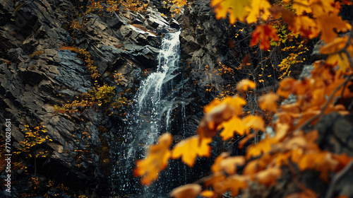 A narrow waterfall streaming down a vertical rock face surrounded by autumn-colored foliage. © Finsch