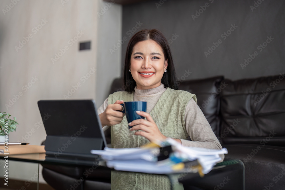 Happy young asian freelance business woman sitting on the floor at home working on digital tablet while drinking coffee Happy young asian freelance business woman sitting on the floor at home working on digital tablet while drinking coffee