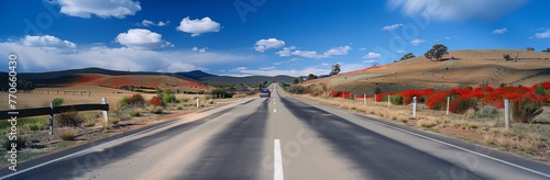 A car is driving down a long, empty road with a clear blue sky above