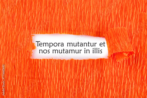 Tempora mutantur et nos mutamur in illis Translated from Latin, it means Times are changing, and we are changing with them. on a white sheet under an orange background photo