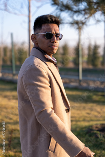 Картината върху платно A man wearing a tan coat and sunglasses stands in a grassy field