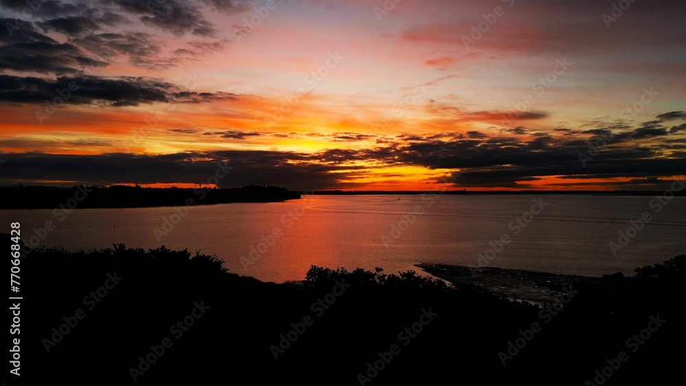 Orange sunset casts a reflective glow upon the tranquil Bucklands Beach, Auckland, New Zealand