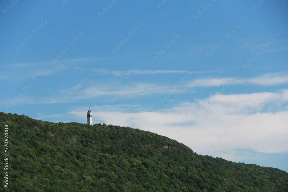 Scenic view of a lighthouse atop a grassy hill on the background of the blue sky Scenic view of a lighthouse atop a grassy hill on the background of the blue sky