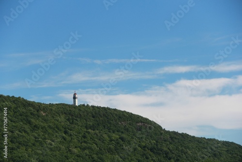 Scenic view of a lighthouse atop a grassy hill on the background of the blue sky