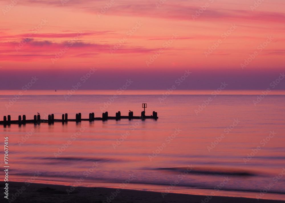Scenic view of a pier on a tranquil sea at pink sunset