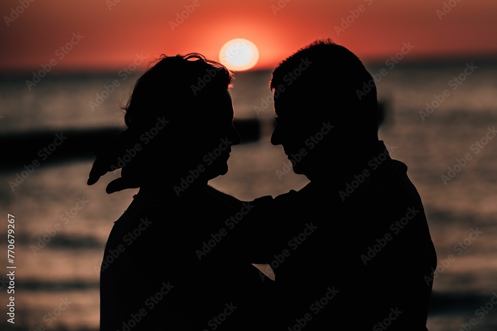 Mature couple on a beach silhouetted against the background of the sky at sunset.