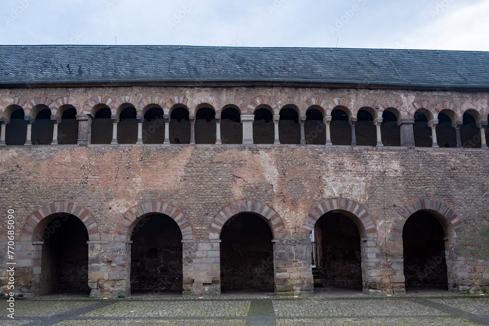 Captured in Trier, Germany, this image exhibits the Romanesque revival with its series of arches from the Imperial Palace. The beige and brown stonework against an overcast sky highlights the timeless Captured in Trier, Germany, this image exhibits the Romanesque revival with its series of arches from the Imperial Palace. The beige and brown stonework against an overcast sky highlights the timeless