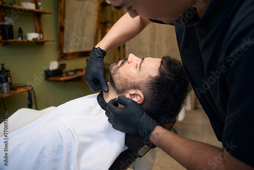 Barber trimming man's beard in barbershop