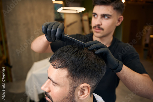Man coiffeur making hairstyle for bearded customer