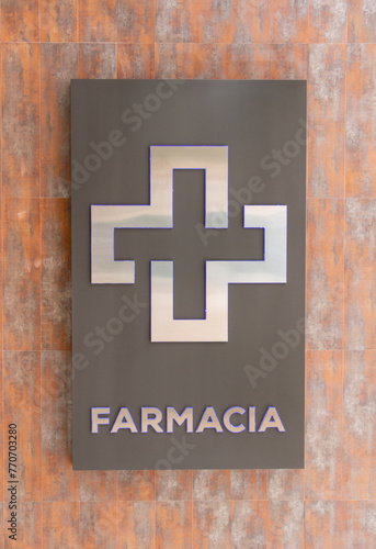Spanish logo "Farmacia". English : drugstore. Metallic sign on a ceramic wall.
