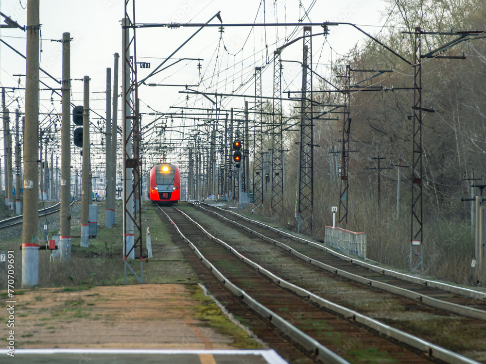 Electric transport on the railway. Contact power lines for commuter trains. A modern urban electric train on the railway tracks. Transportation of passengers within the city limits. - obrazy, fototapety, plakaty 