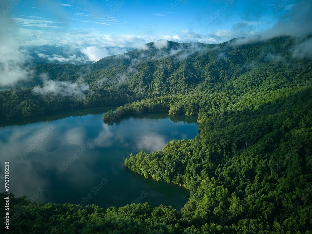 a lake surrounded by greenery covered in low clouds with mountains behind