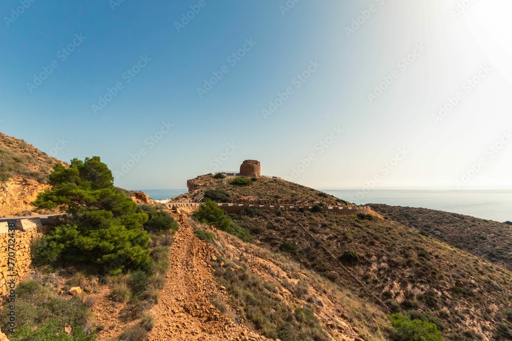 Clear dirt road leading down towards a picturesque hill and a quaint building in Benidorm - obrazy, fototapety, plakaty 
