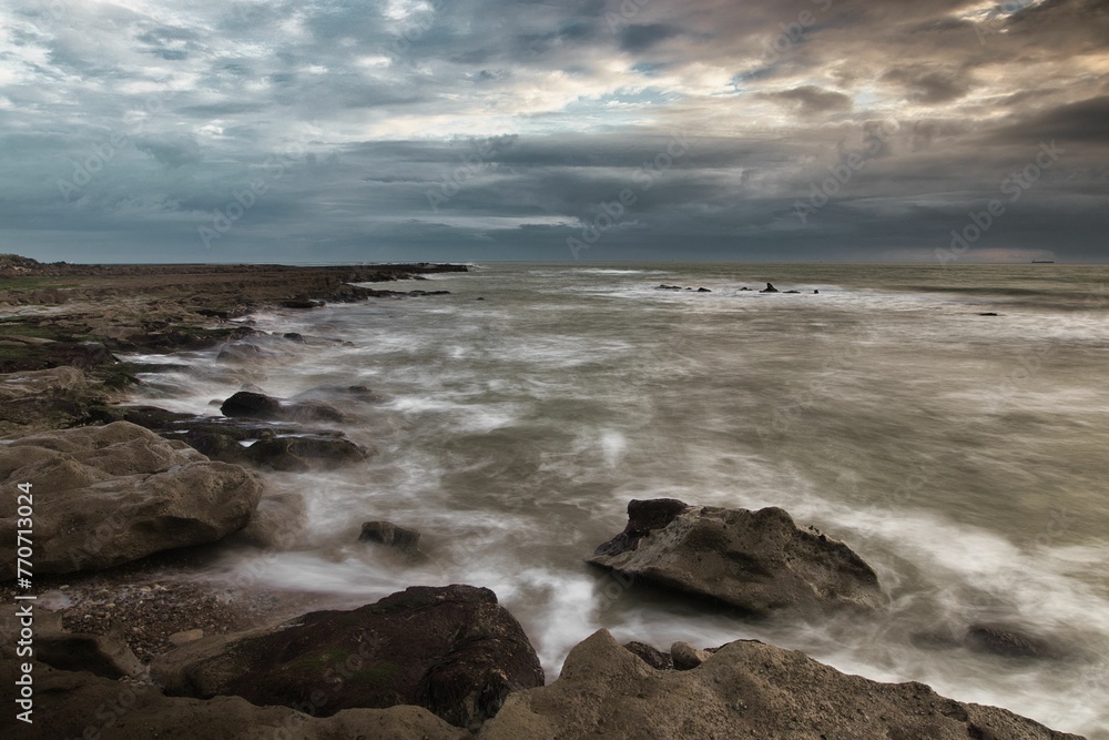Ocean flowing along the rocky shore as a cloudy sky hangs over the horizon, Isle of Wight