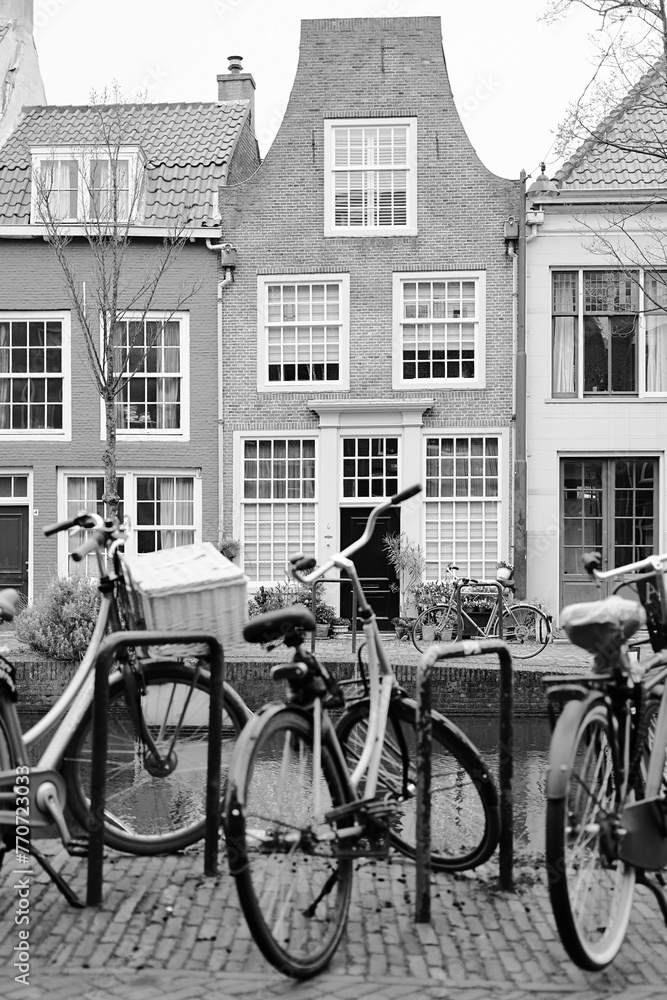 Picturesque Netherlands in black and white. Bicycles parked alongside a channel on beautiful old buildings background.