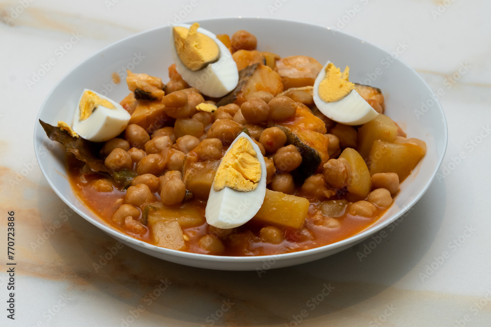 lent stew: a plate of chickpeas with pepper, potatoes and cod with tomato and hard-boiled egg on a white veined marble table lent stew: a plate of chickpeas with pepper, potatoes and cod with tomato and hard-boiled egg on a white veined marble table