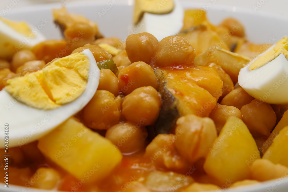 Lenten stew: detail of a plate of chickpeas with pepper, potatoes and cod with tomato and a bay leaf and hard-boiled egg on a white veined marble table Lenten stew: detail of a plate of chickpeas with pepper, potatoes and cod with tomato and a bay leaf and hard-boiled egg on a white veined marble table