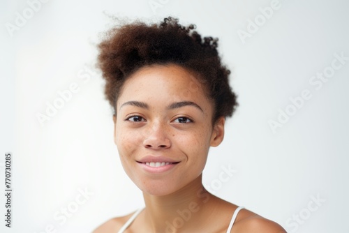 Young woman with natural hair and freckles  wearing a white tank top  looking calmly at the camera.