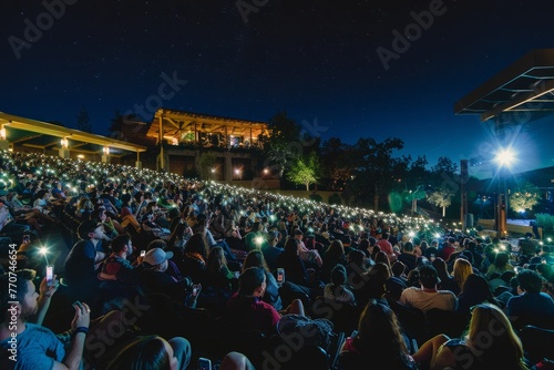 A wide-angle shot from the stage captures a large crowd of people holding up their cell phones
