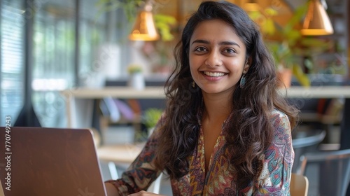 Closeup portrait of a smiling young South Asian woman working on a laptop © Raveen