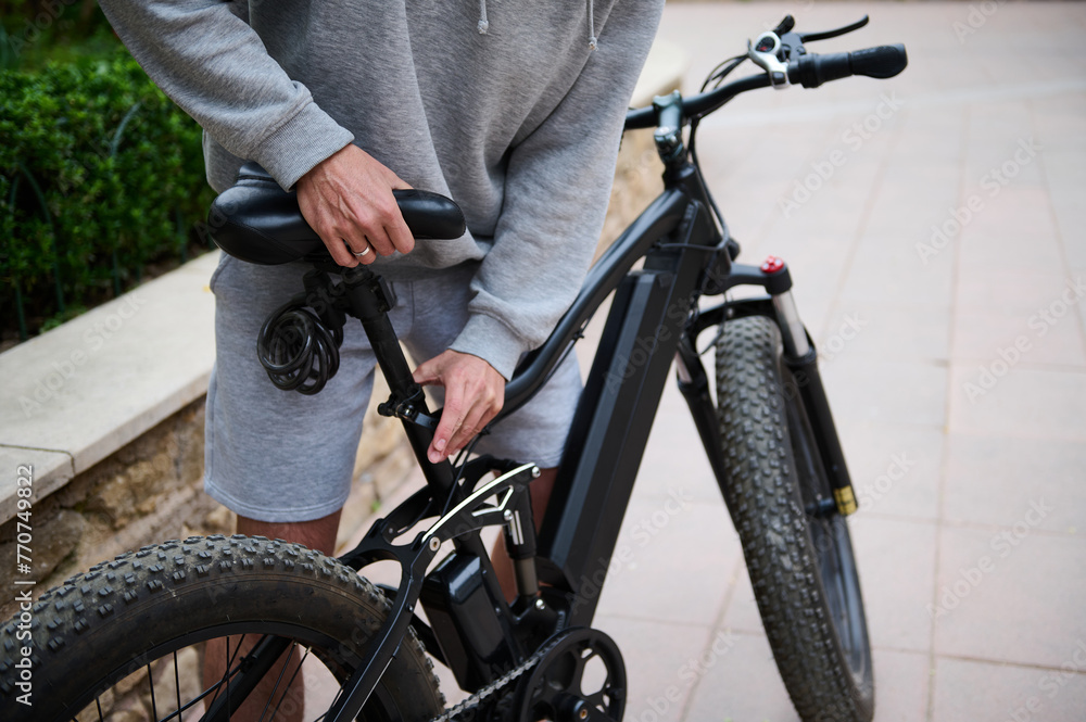 Cropped view man cyclist adjusting a seat on an electric motor bike while renting e-bike as eco-friendly urban transport Cropped view man cyclist adjusting a seat on an electric motor bike while renting e-bike as eco-friendly urban transport