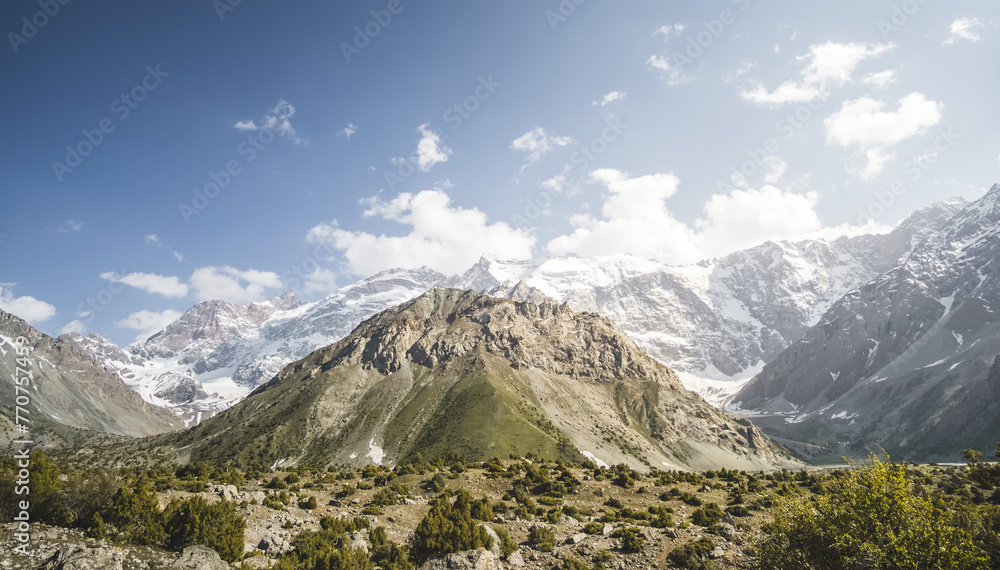 Fototapeta premium Mountain panoramic landscape of the Fan Mountains with rocks, glaciers and vegetation in sunny weather with blue sky, mountain panorama in Tajikistan in the early evening