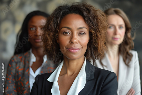 Front view of a composed businesswoman with her determined team in the background, portraying strong leadership.