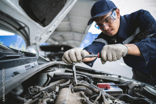 A mechanic is working on a car engine. He is wearing a blue shirt and a blue hat © KANGWANS