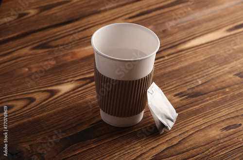 Cardboard cup for hot drinks and tea bag on wooden background