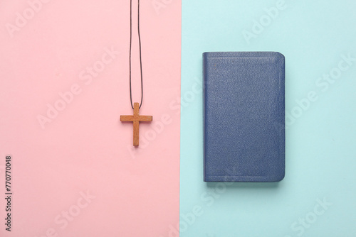Bible book and wooden Christian cross on a string, pink blue background photo