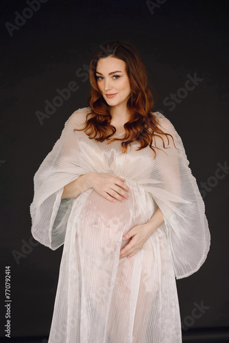 Attractive pregnant woman in ivory dress posing in the studio on black background photo